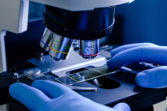 A vertical closeup shot of a laboratory worker working with a modern microscope while conducting a coronavirus research